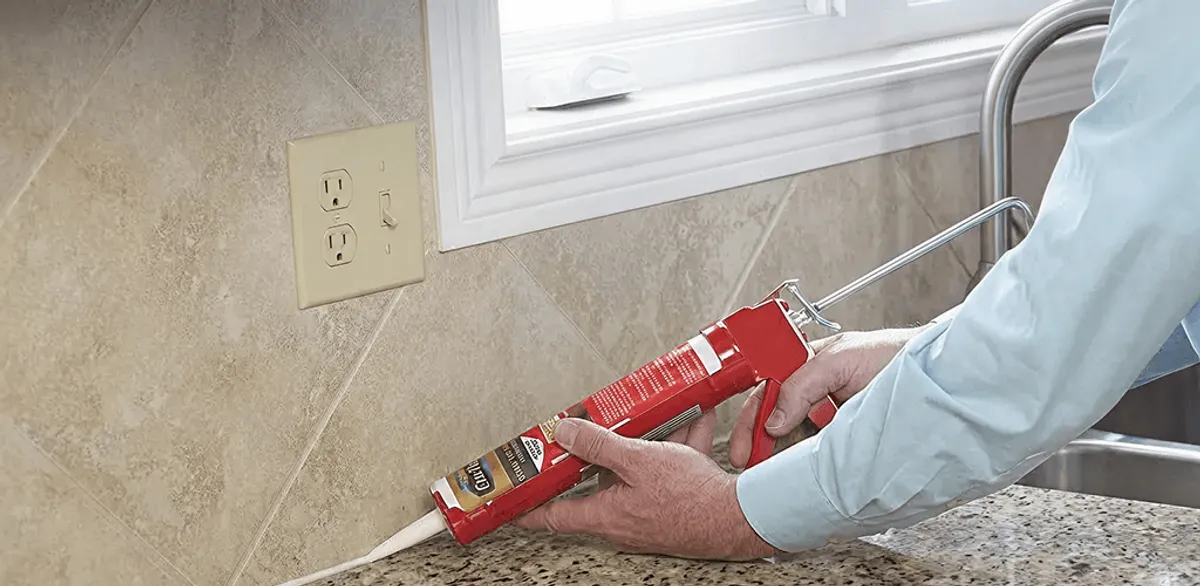 Handyman applying caulk along a kitchen backsplash and countertop seam in Toledo, OH